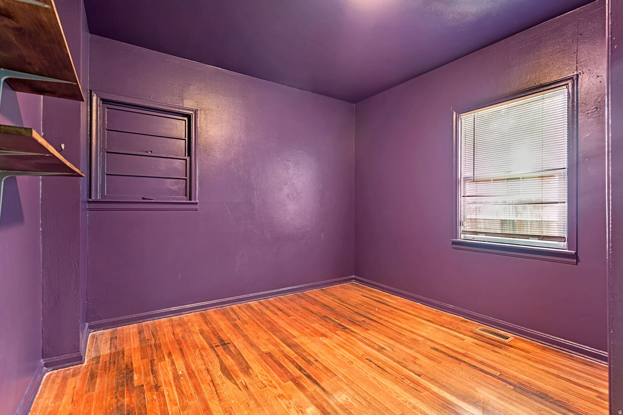 Room with wood-finish flooring, purple painted walls and ceiling, two windows with trim, and built-in shelving