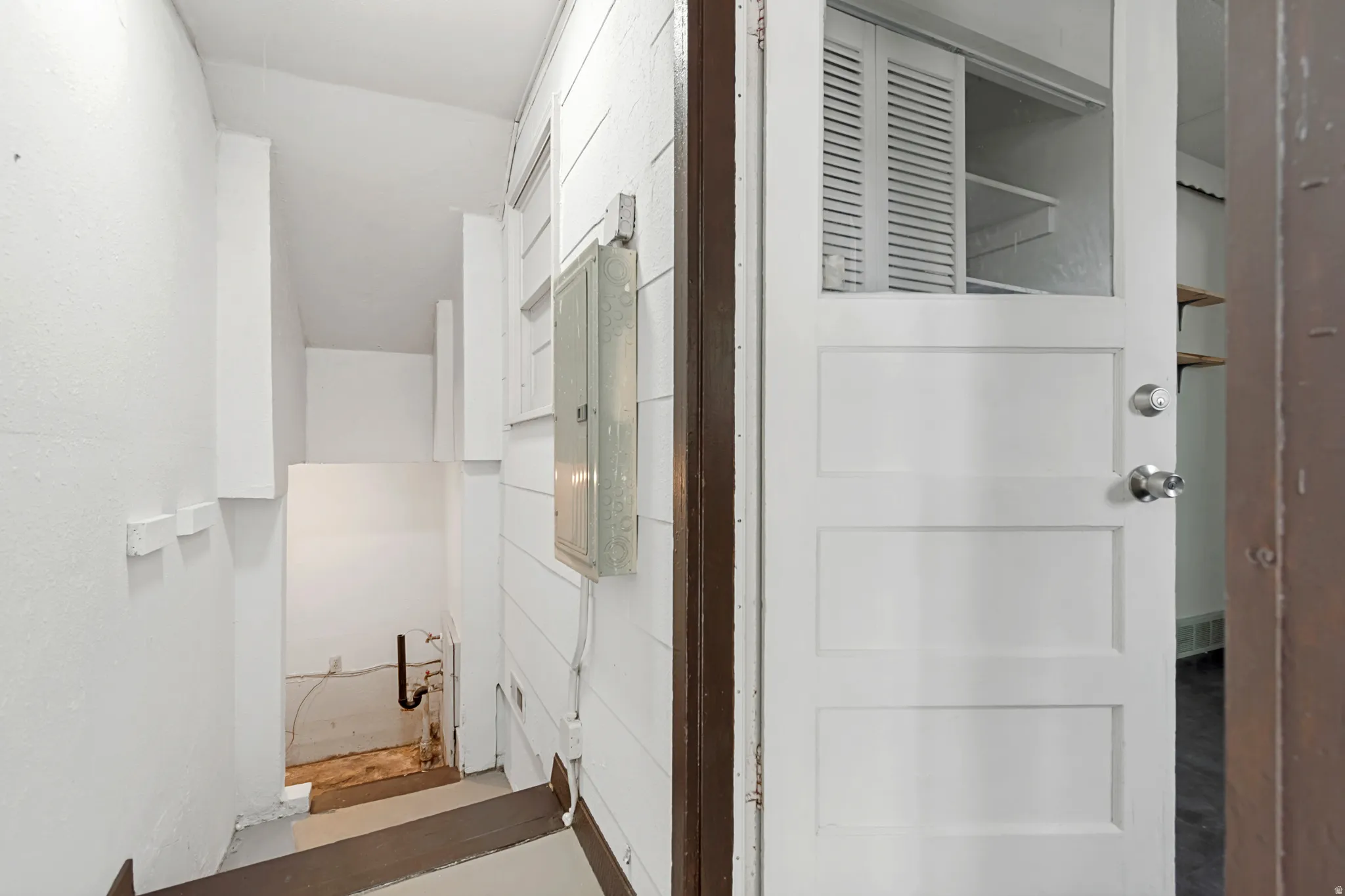 Utility area featuring a panel door with clear pane, a utility panel, and white shiplap wall finishes