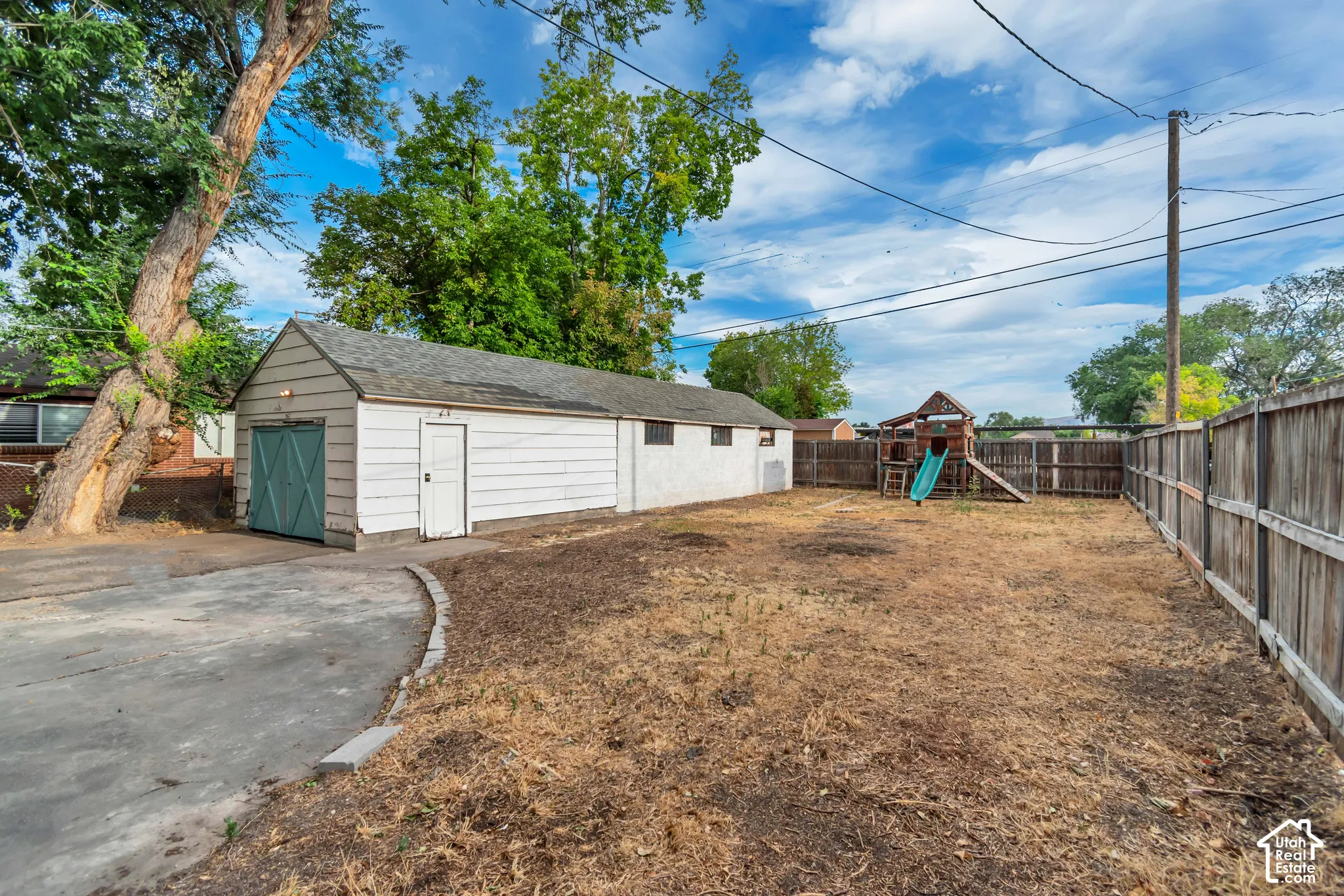 Expansive outdoor area featuring a detached garage with double doors, concrete driveway, and a wood privacy fence