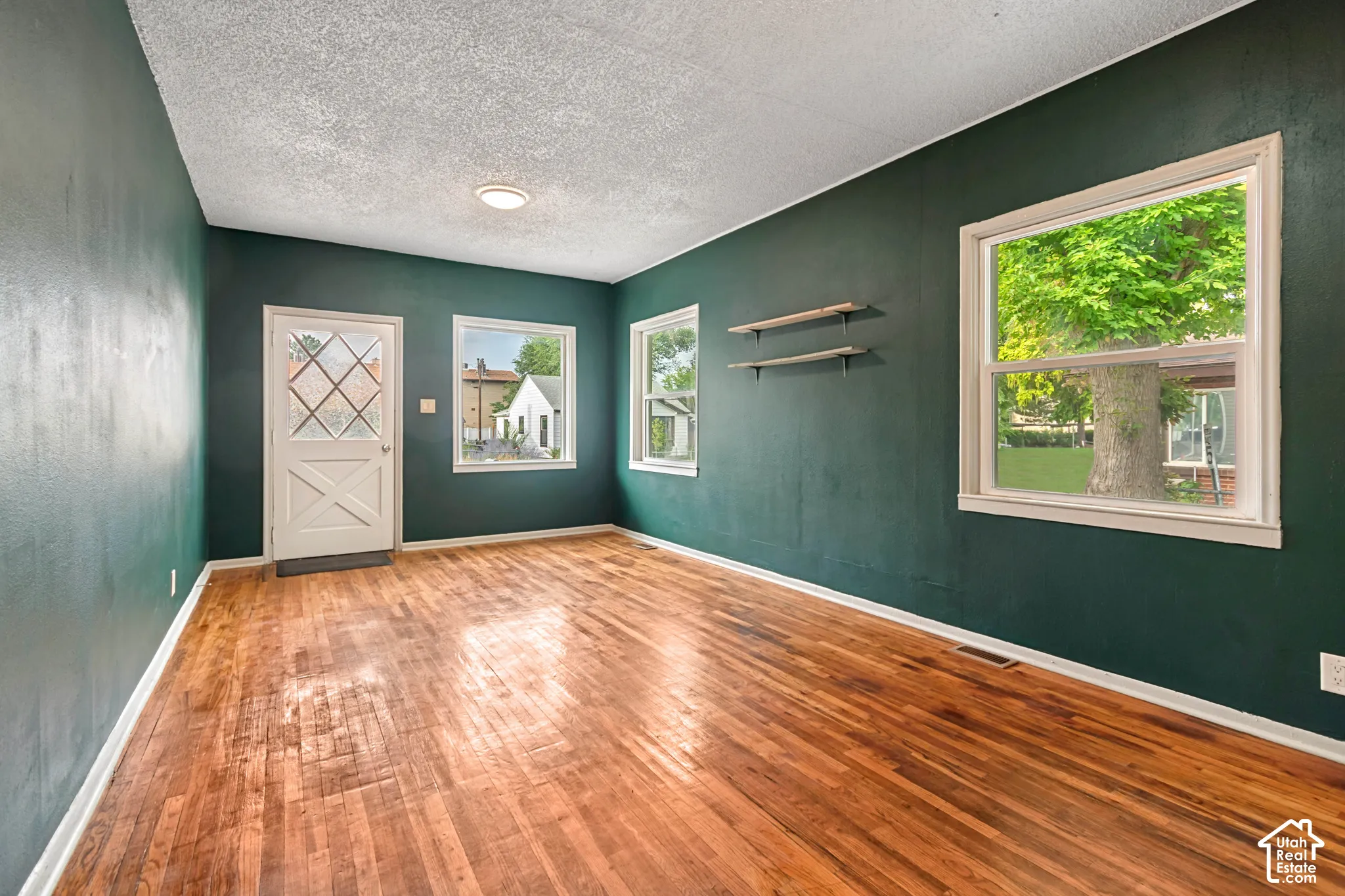 Hardwood flooring throughout a room with deep green painted walls and white trim