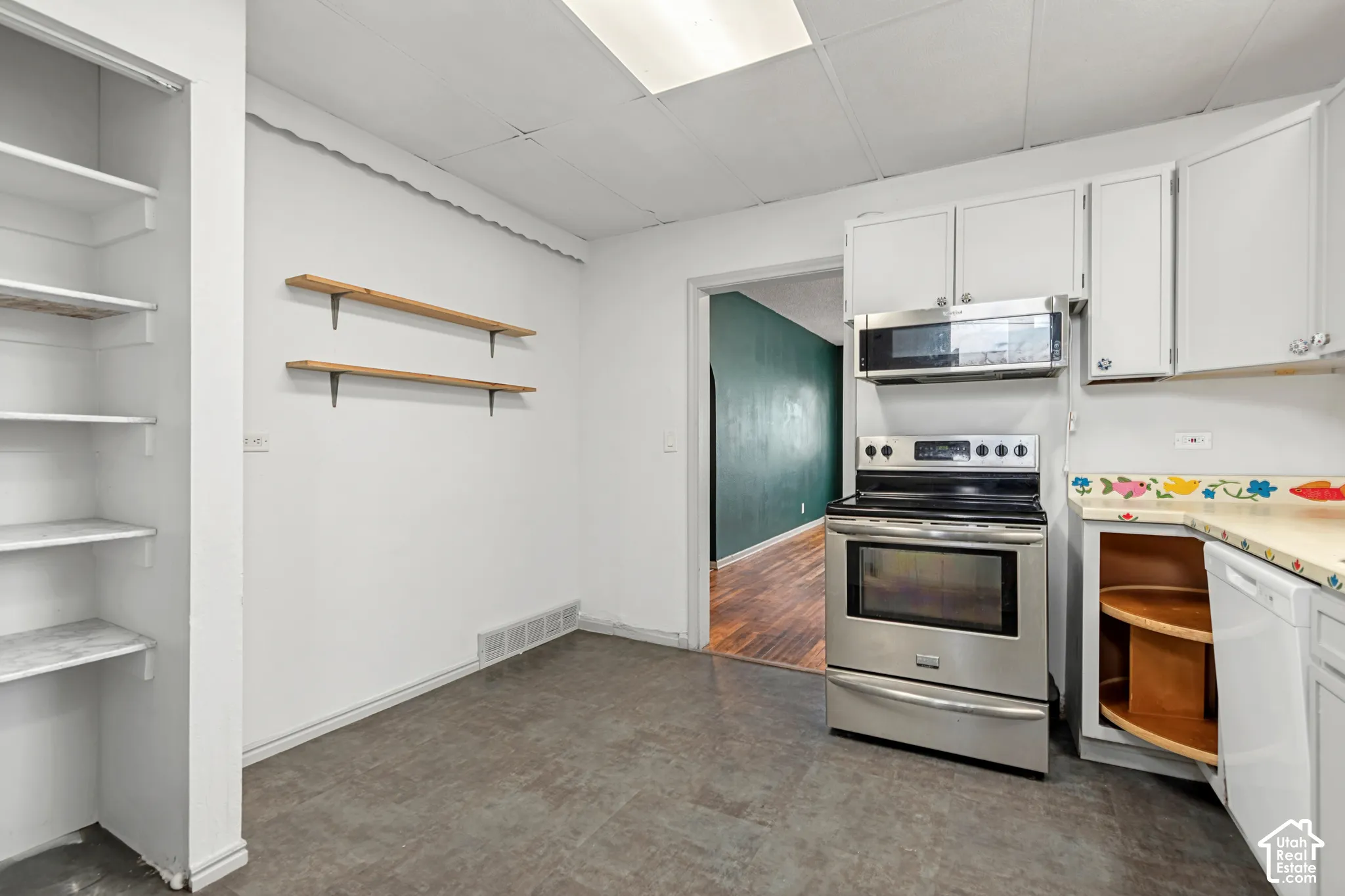 Kitchen featuring stainless steel range, stainless steel microwave, white cabinetry, and gray flooring
