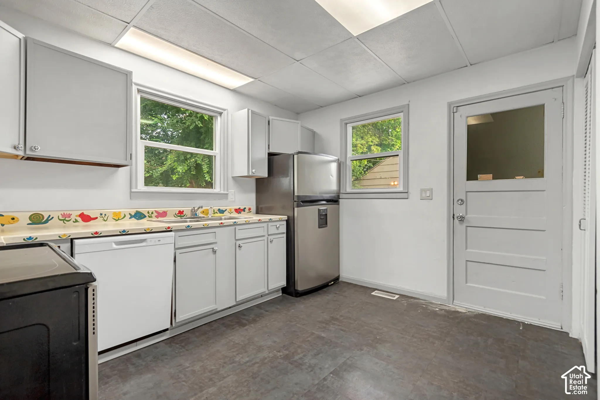 Kitchen featuring white cabinetry, a built-in dishwasher, stainless steel refrigerator, dark flooring, and two windows