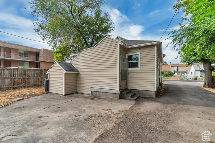 Exterior featuring beige horizontal siding, a detached storage shed with matching siding, concrete paving, and mature perimeter trees