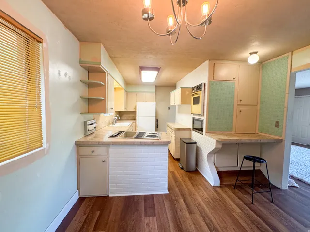 Kitchen featuring wood-finish flooring, white brick-patterned bar area, built-in wall oven and microwave, and a counter-height dining surface