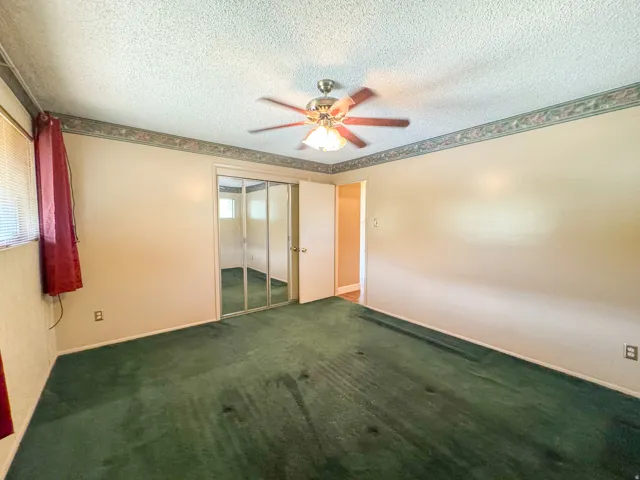 Bedroom featuring wall-to-wall green carpeting, neutral painted walls, and a textured ceiling
