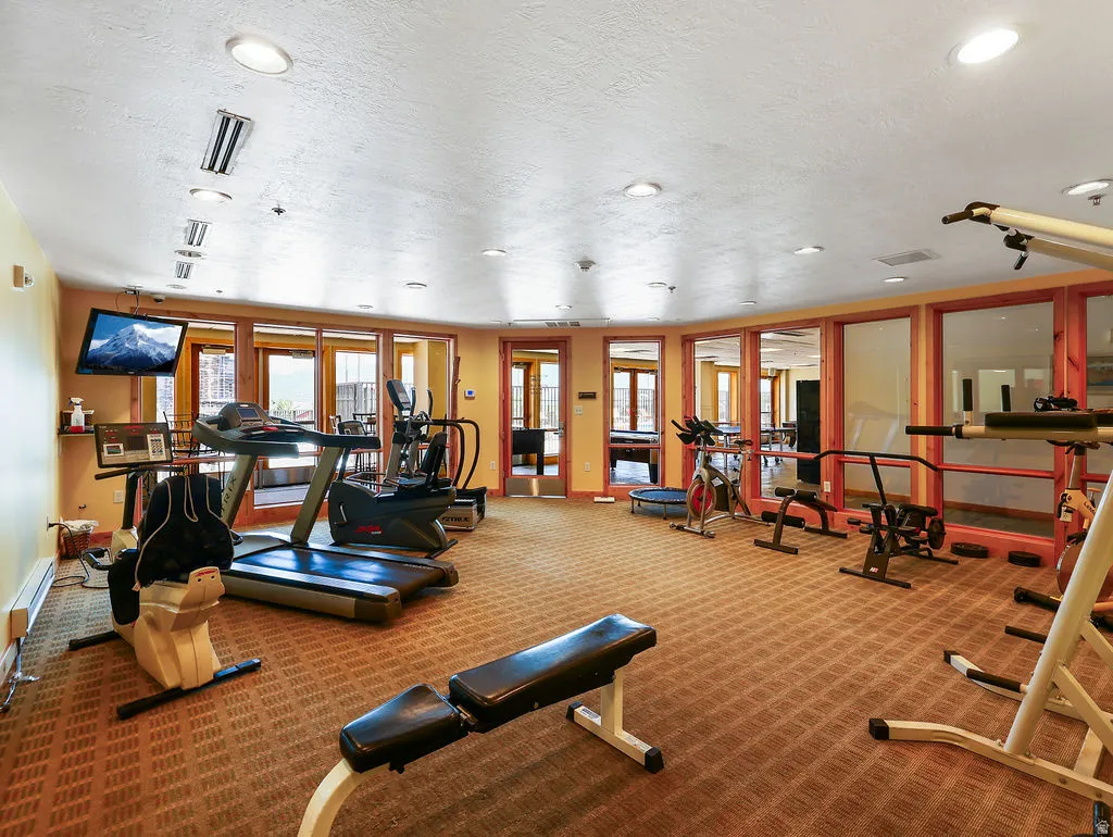 Dedicated fitness area featuring patterned carpet flooring, recessed lighting, and a wall-mounted television