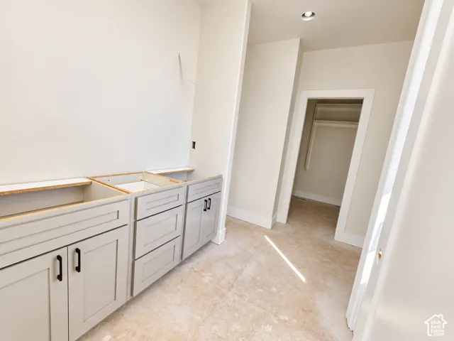 Light-toned floor tiling, shaker-style cabinetry with matte black hardware, recessed ceiling lighting, and a walk-in closet