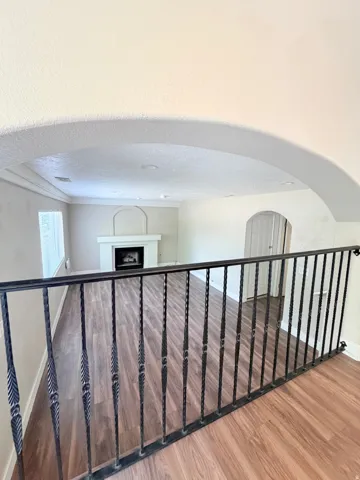 Interior balcony with wrought iron railing overlooking a living space featuring laminate wood-finish flooring, a white fireplace with an arched mantel, and recessed lighting