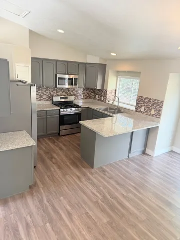 Kitchen featuring wood-finish flooring, grey cabinetry, granite-style countertops, mosaic tile backsplash, and stainless steel appliances