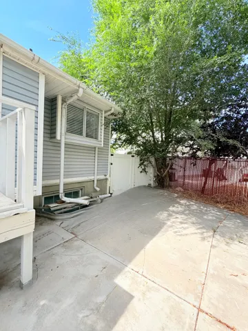 Paved concrete patio featuring a white privacy fence and mature trees