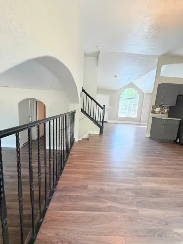 Open-concept interior featuring wood-finish flooring, a wrought iron railing, and arched architectural details