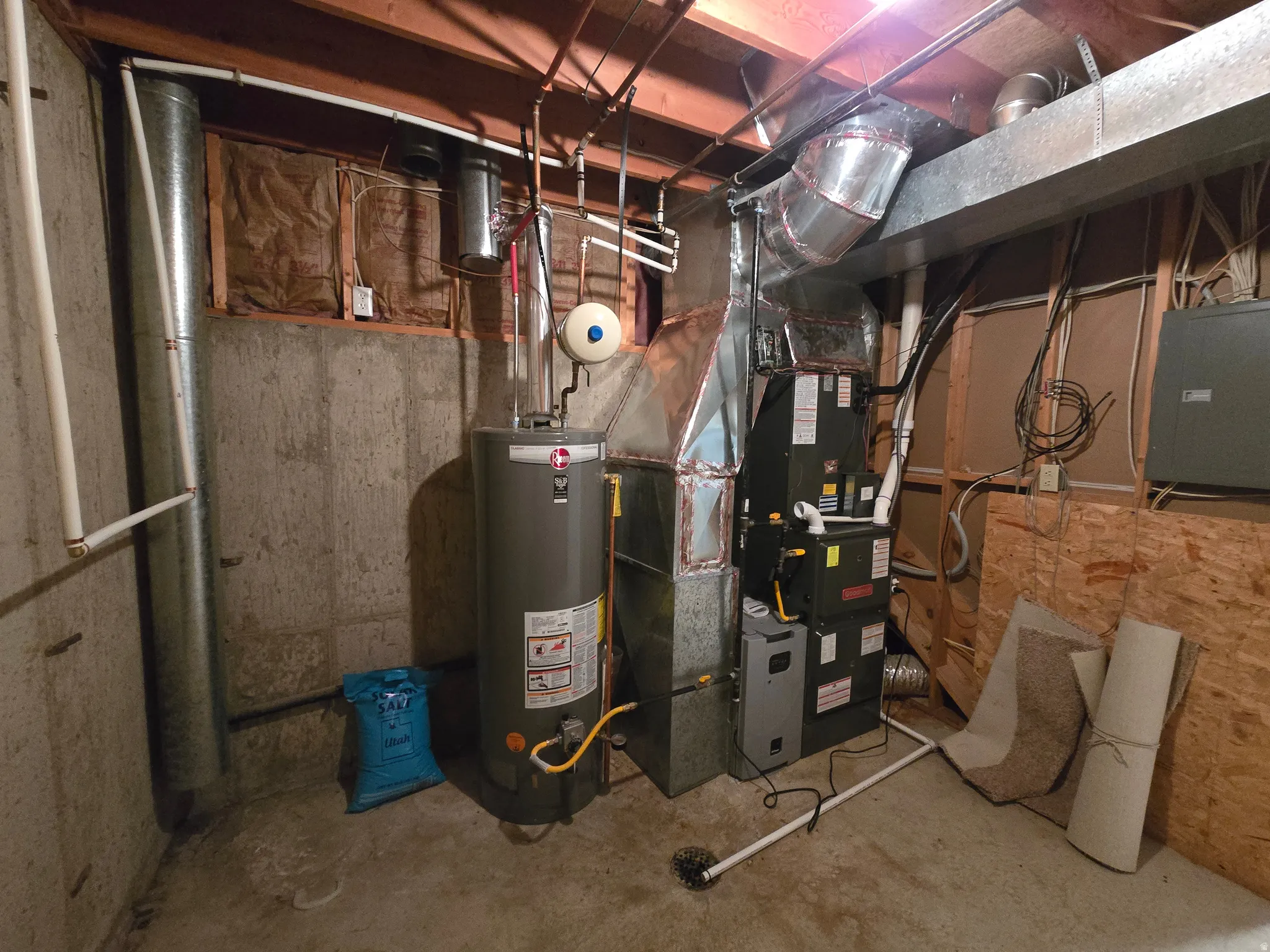 Utility space featuring a water heater, furnace system, concrete floor, exposed wood ceiling joists, and visible ductwork