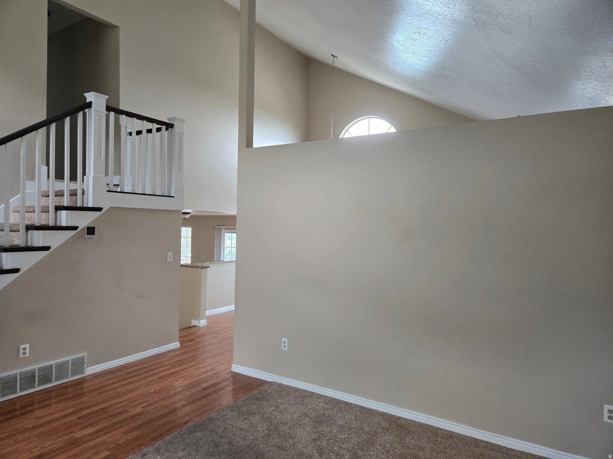 Vaulted ceilings with an arched window and a staircase featuring white newel posts and dark wood-finish handrails