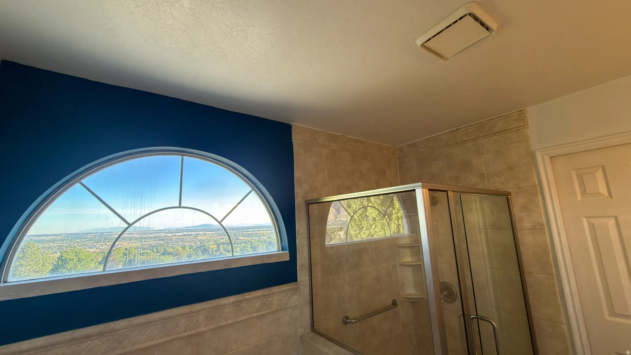 Arched transom window with exterior scenery, tiled shower enclosure with glass door, and a built-in shower shelf