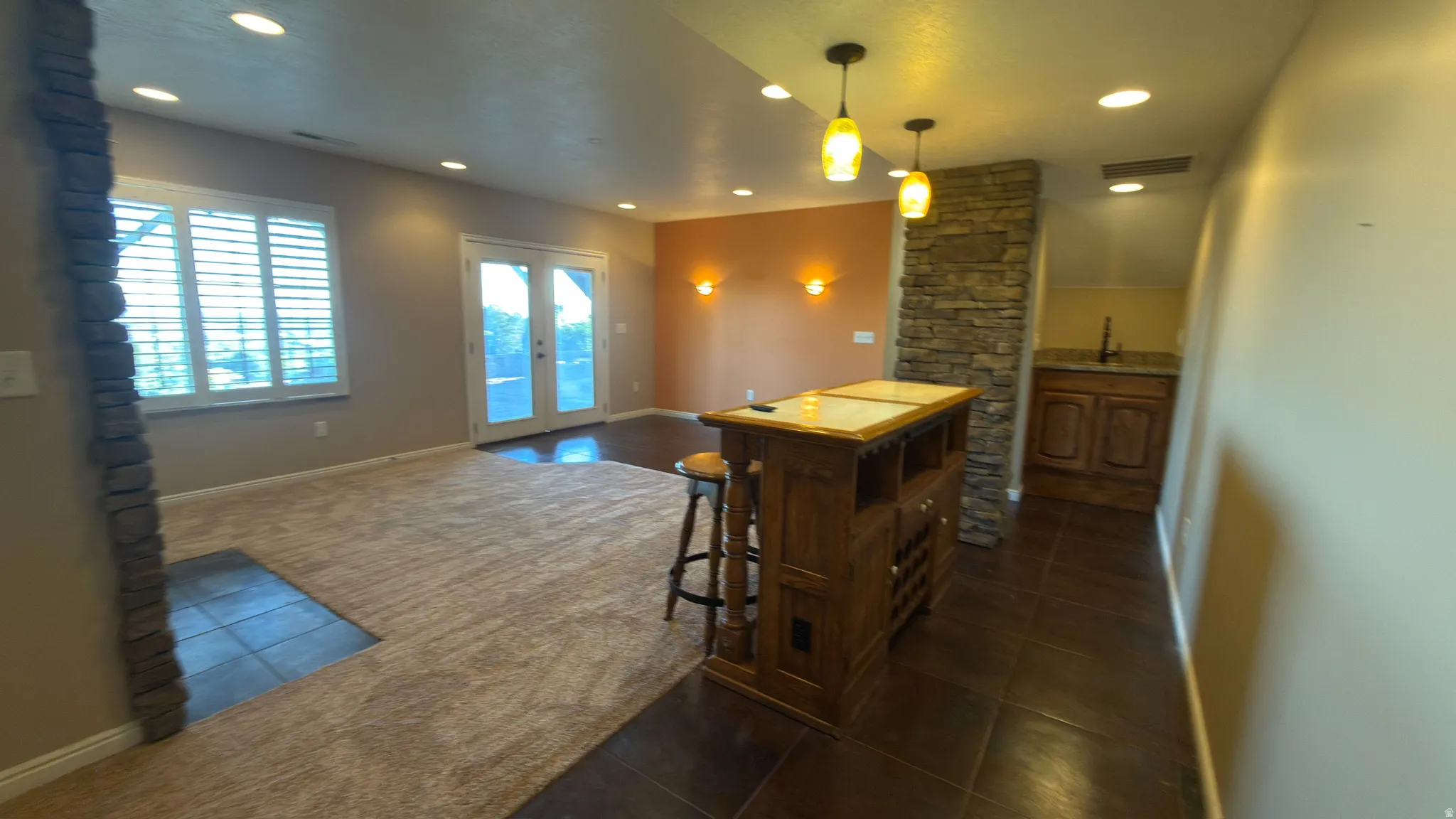 Spacious area featuring plush carpeting, a stone-wrapped column, and a built-in wet bar with wood cabinetry and a countertop