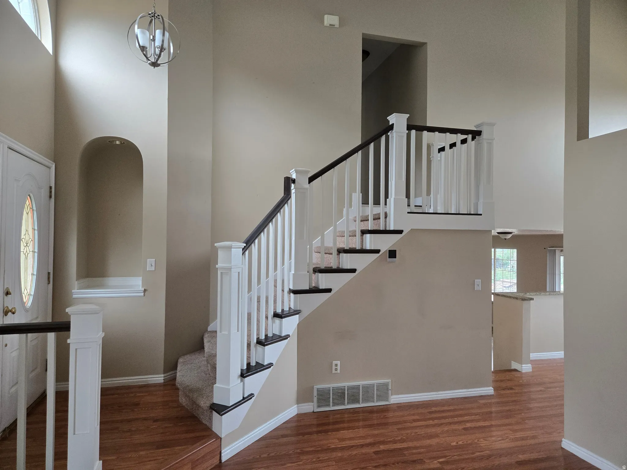 Two-story entry featuring wood-finish flooring, a carpeted staircase with white and dark wood railings, an arched wall niche, and a contemporary chandelier