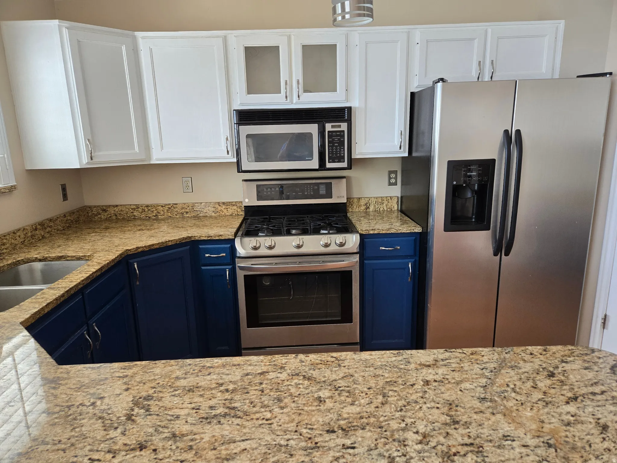 Kitchen featuring two-tone cabinetry with white upper and blue base cabinets, stainless steel appliances including a gas range and side-by-side refrigerator, and speckled granite countertops