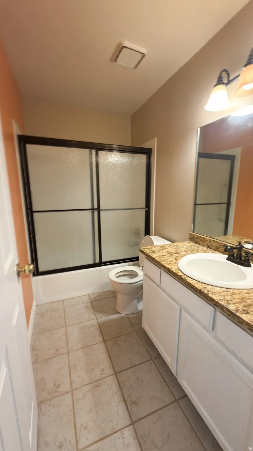 Main bathroom featuring a shower-tub combination with sliding opaque glass doors, a vanity with a granite-style countertop and integrated sink, white base cabinetry, and tile flooring