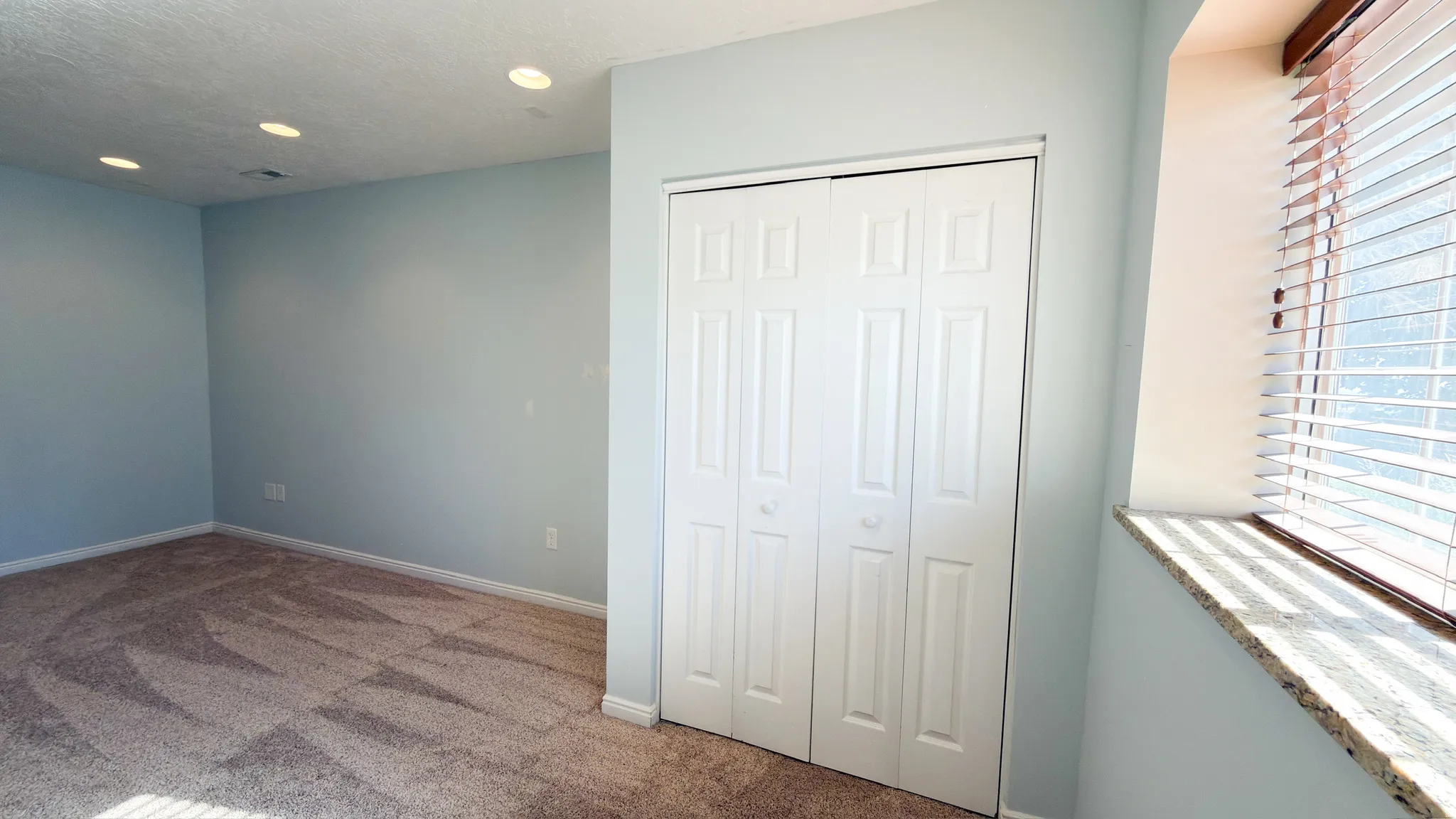 Bright room featuring neutral carpet flooring, recessed lighting, and a window with blinds and a stone sill