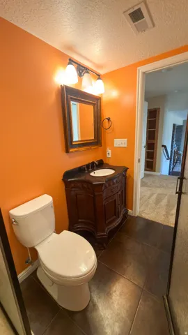Bathroom with a pedestal sink vanity, framed mirror, wall-mounted lighting fixture, and a white toilet