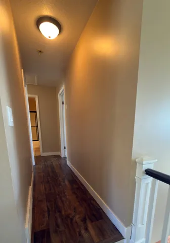 Hallway featuring wood-finish flooring, light tan walls, white baseboards, and a flush-mount ceiling light