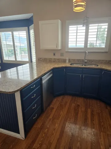 Kitchen featuring wood-finish flooring, dark blue lower cabinetry, light-colored countertops, and a stainless steel dishwasher