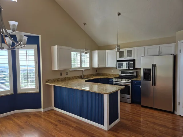 Kitchen featuring vaulted ceilings, wood-finish flooring, granite countertops, stainless steel appliances, and white cabinetry with blue lower cabinets and island base