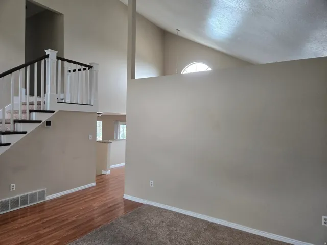 Vaulted ceilings with an arched window and a staircase featuring white newel posts and dark wood-finish handrails
