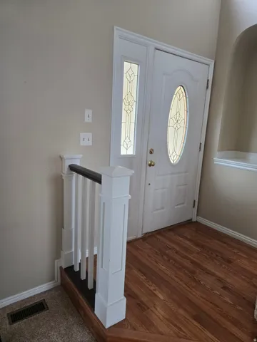 Entryway featuring a white door with an oval decorative glass insert, a coordinating sidelight, wood-finish flooring, and a white balustrade