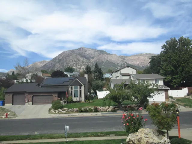 Mountain backdrop, residential street, established landscaping, prominent two-car garage, mature trees