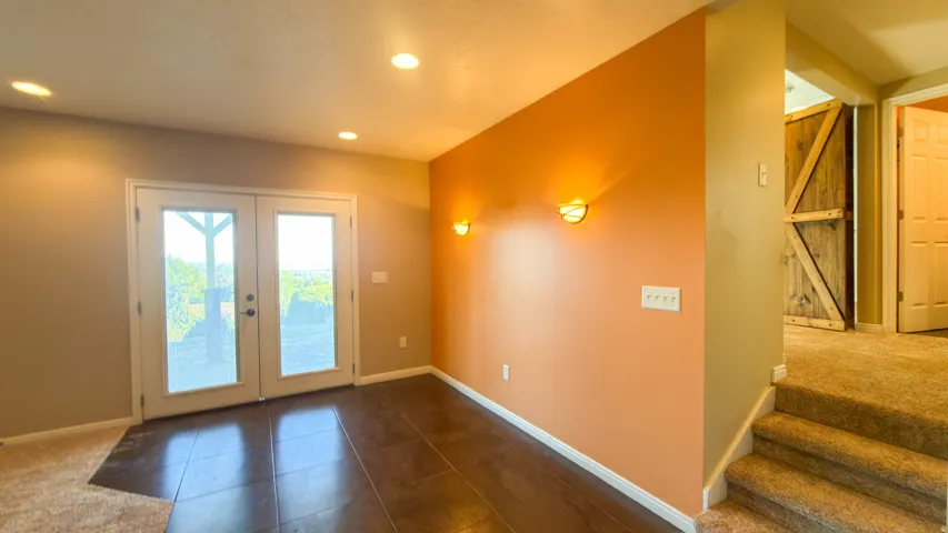 French doors with frosted glass panels, recessed ceiling lighting, wall sconces, wood-finish flooring, and a barn door entry