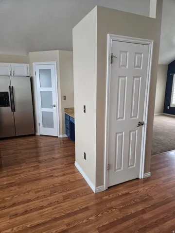 Kitchen area featuring wood-finish flooring, stainless steel refrigerator, white cabinetry, and a frosted glass panel door