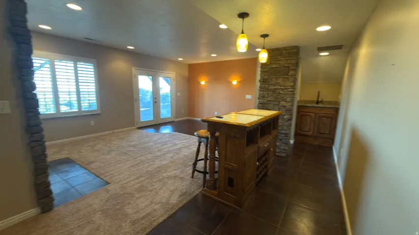 Spacious area featuring plush carpeting, a stone-wrapped column, and a built-in wet bar with wood cabinetry and a countertop