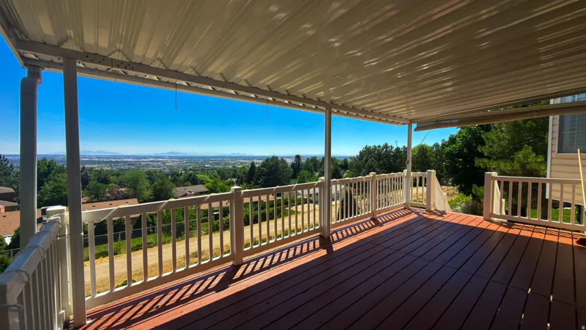 Covered outdoor deck featuring composite decking, white railing, and a distant cityscape backdrop