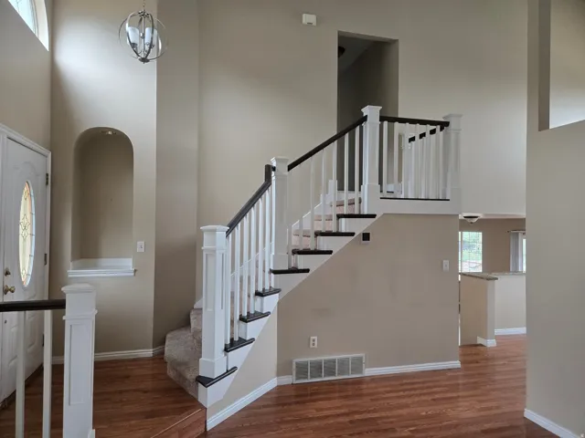 Two-story entry featuring wood-finish flooring, a carpeted staircase with white and dark wood railings, an arched wall niche, and a contemporary chandelier