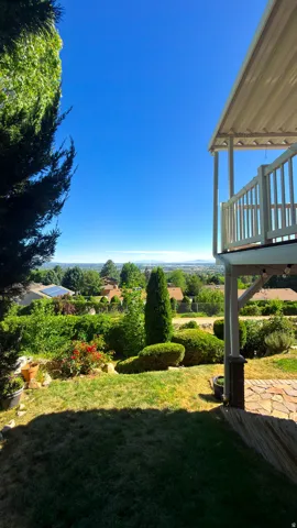 Expansive outdoor space featuring a covered deck with white railing, a stone patio, and a terraced garden with mature landscaping