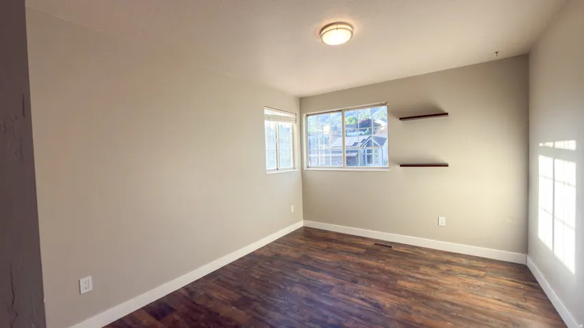 Spacious room featuring wood-finish flooring, two windows, two built-in floating shelves, and a flush-mount ceiling light fixture