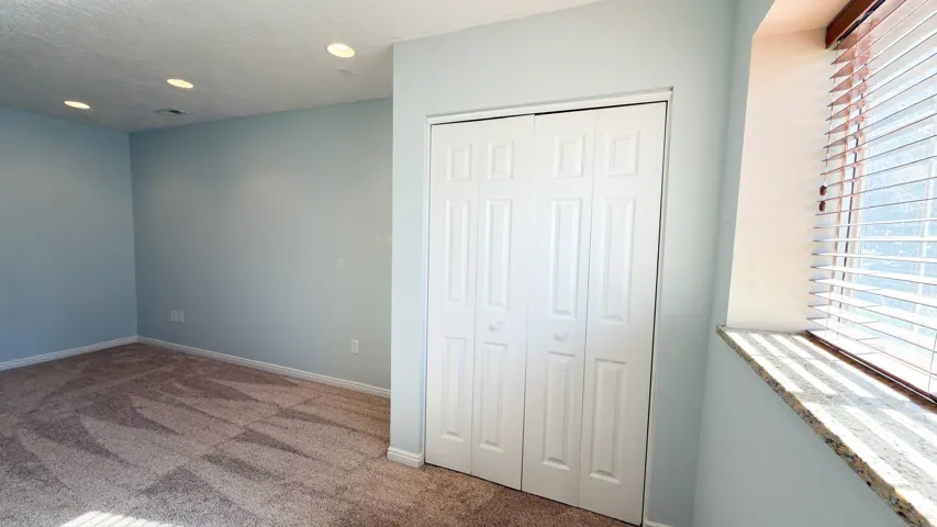 Bright room featuring neutral carpet flooring, recessed lighting, and a window with blinds and a stone sill
