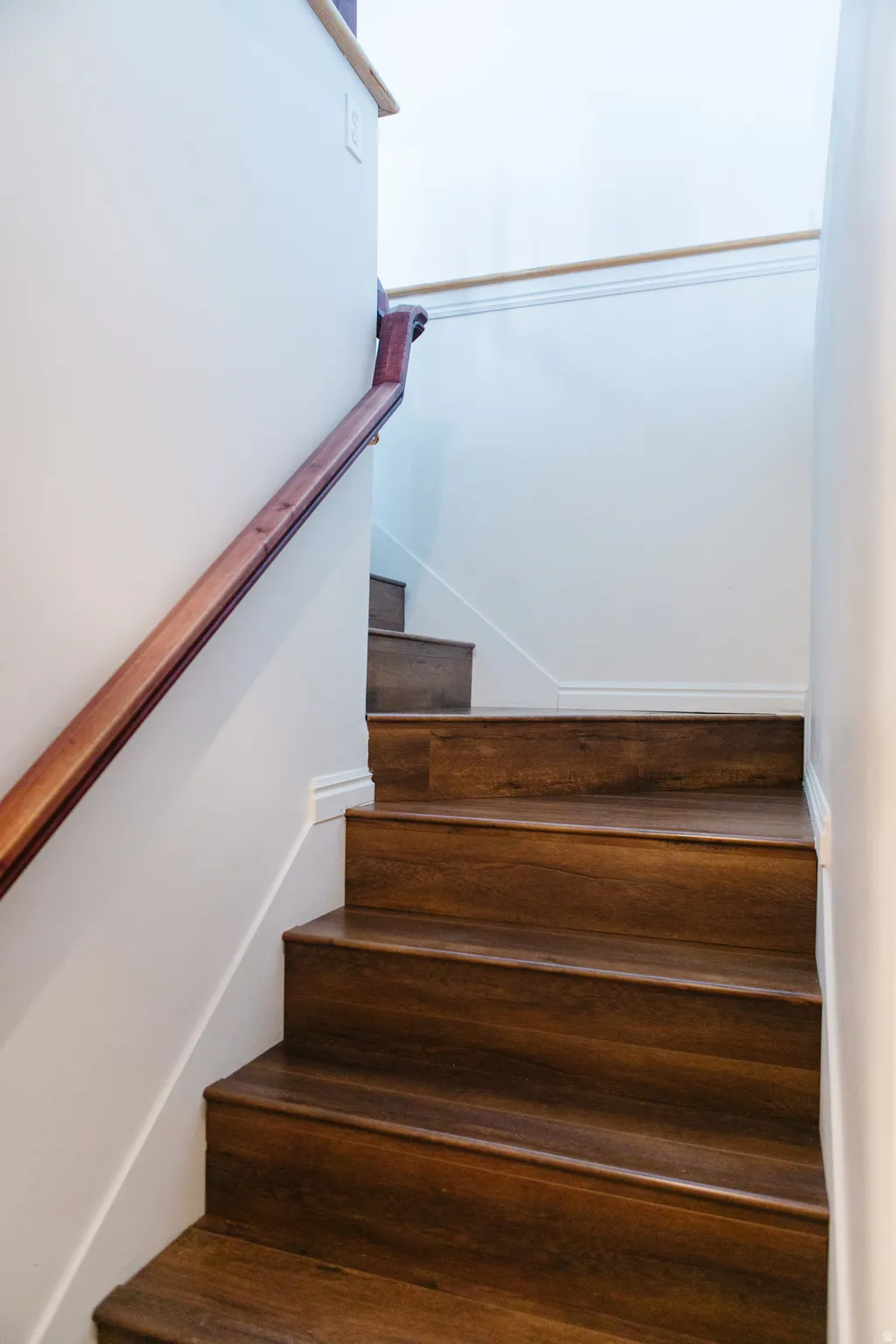 Staircase featuring wood-finish treads and risers, white painted walls, and a contrasting wood handrail