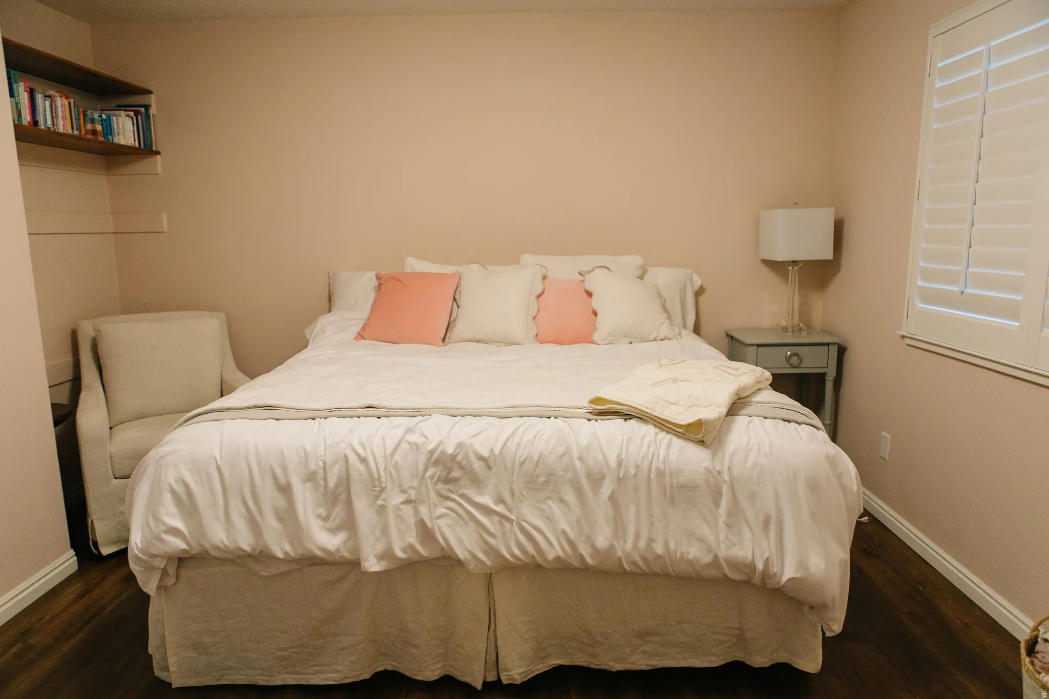 Bedroom with wood-finish flooring, light-colored walls, and white plantation shutters