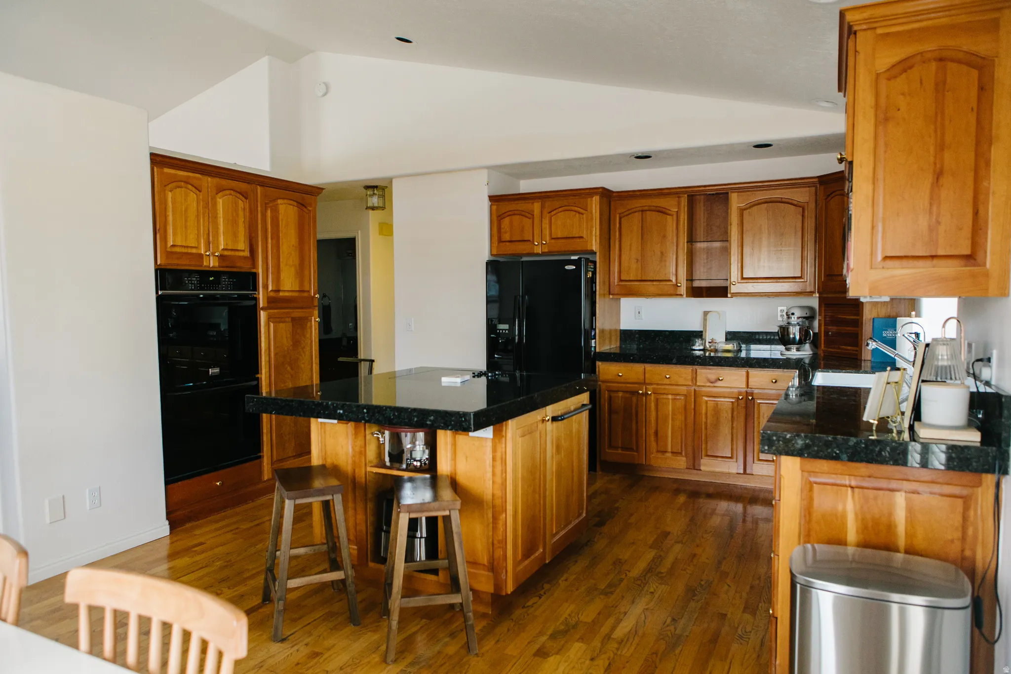 Spacious kitchen featuring warm wood cabinetry, granite countertops, wood-finish flooring, a built-in double oven, and a central island with seating