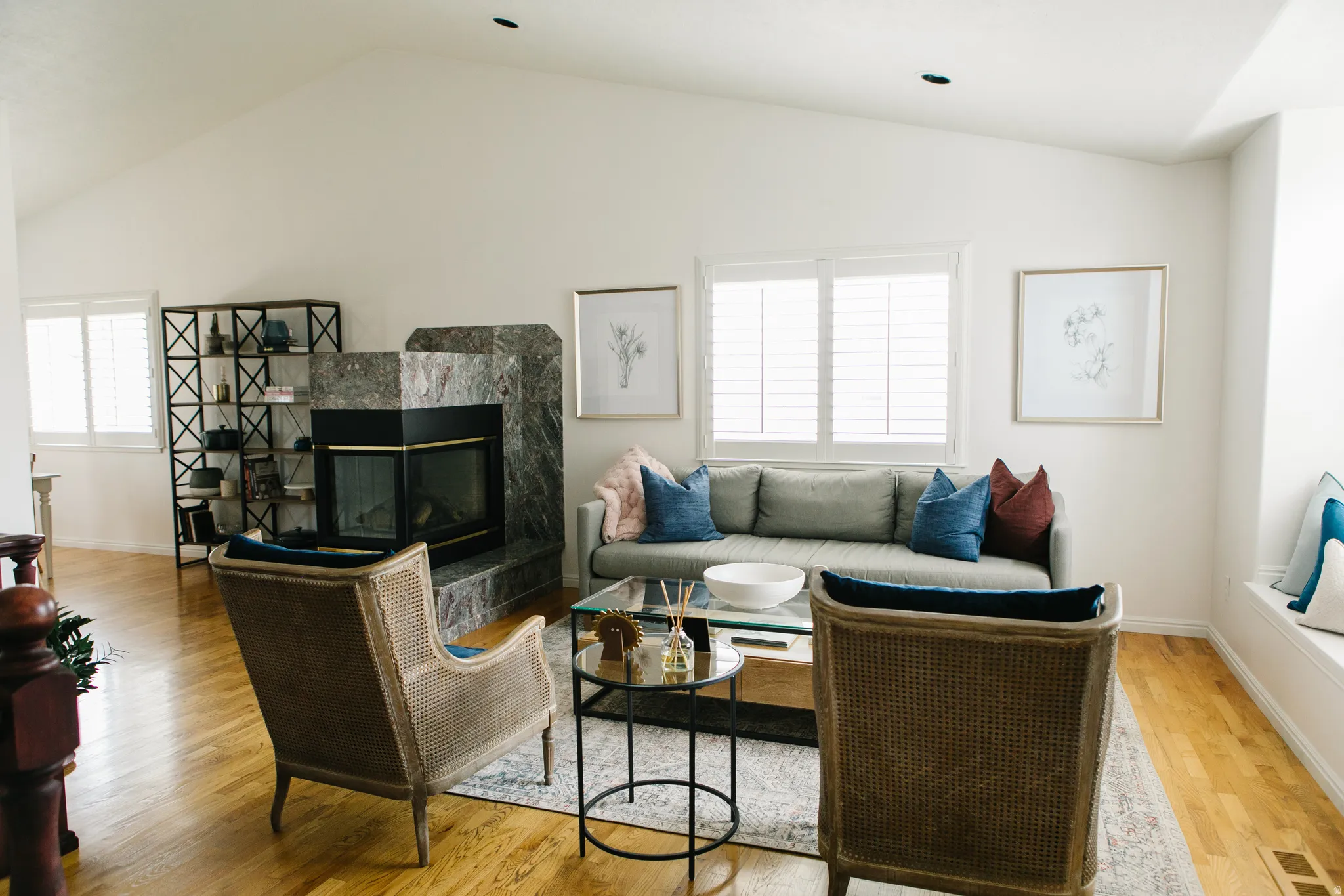 Spacious living area featuring a fireplace with surround, vaulted ceiling, wood flooring, and multiple windows with plantation shutters