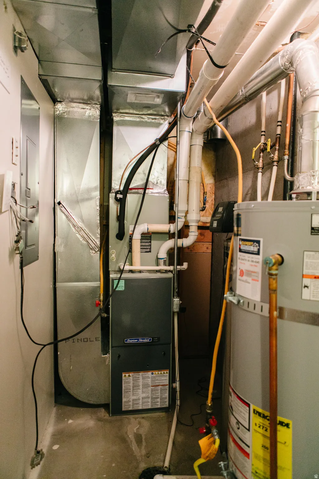 Utility area featuring an American Standard furnace, a water heater, extensive ductwork, and exposed piping