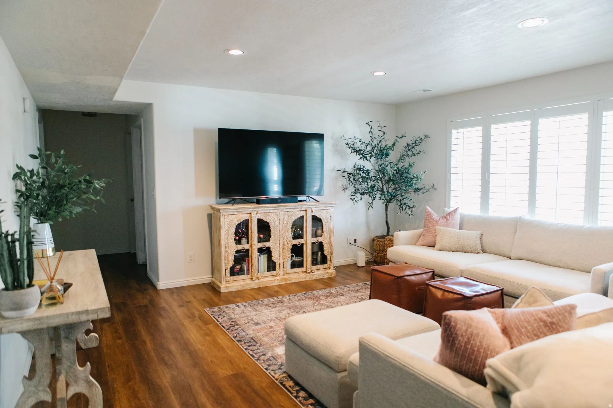 Spacious living area featuring wood-finish flooring, recessed lighting, and a large window with plantation shutters