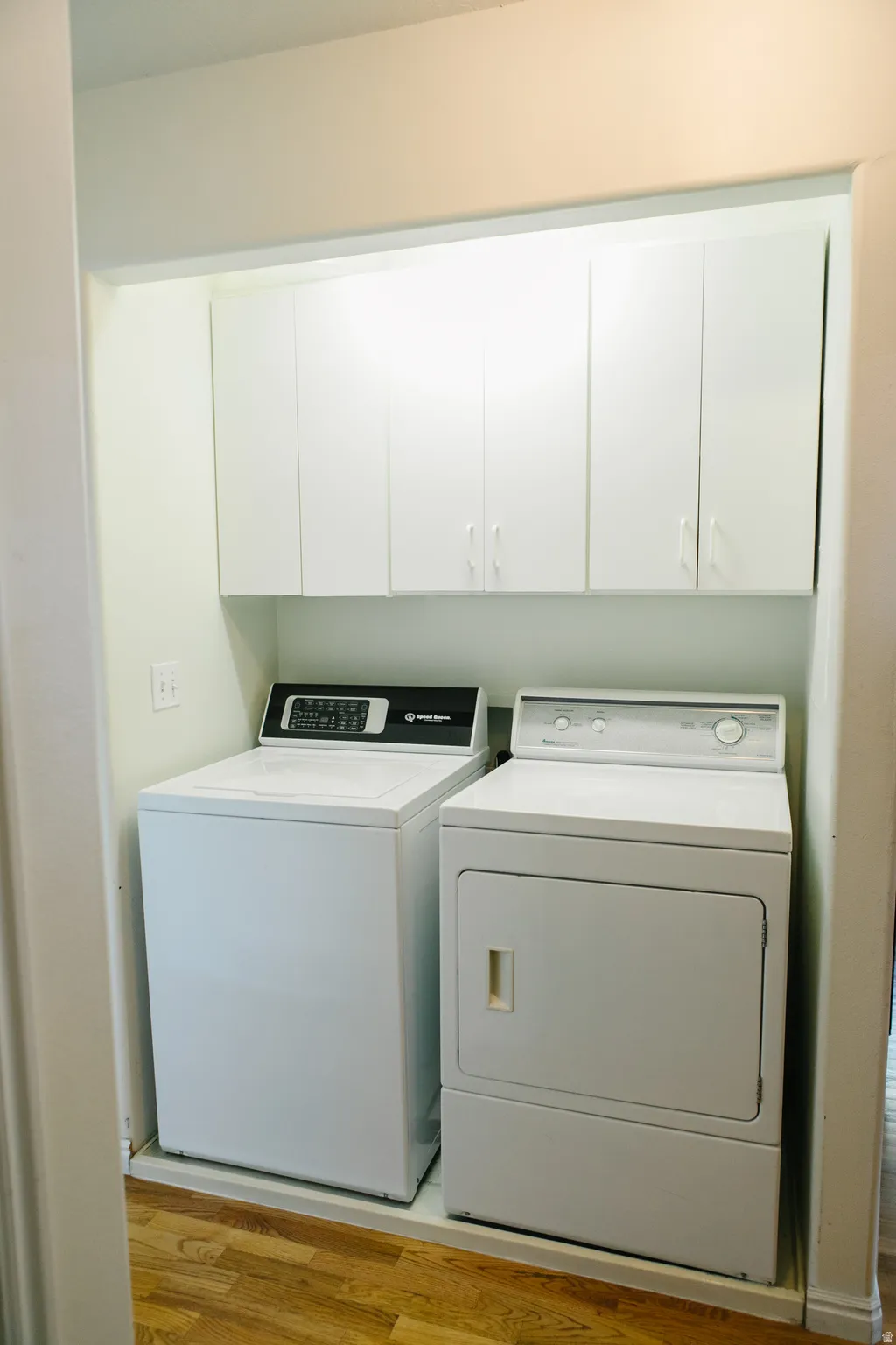 Dedicated laundry area featuring wood flooring, white overhead cabinetry, and recessed lighting