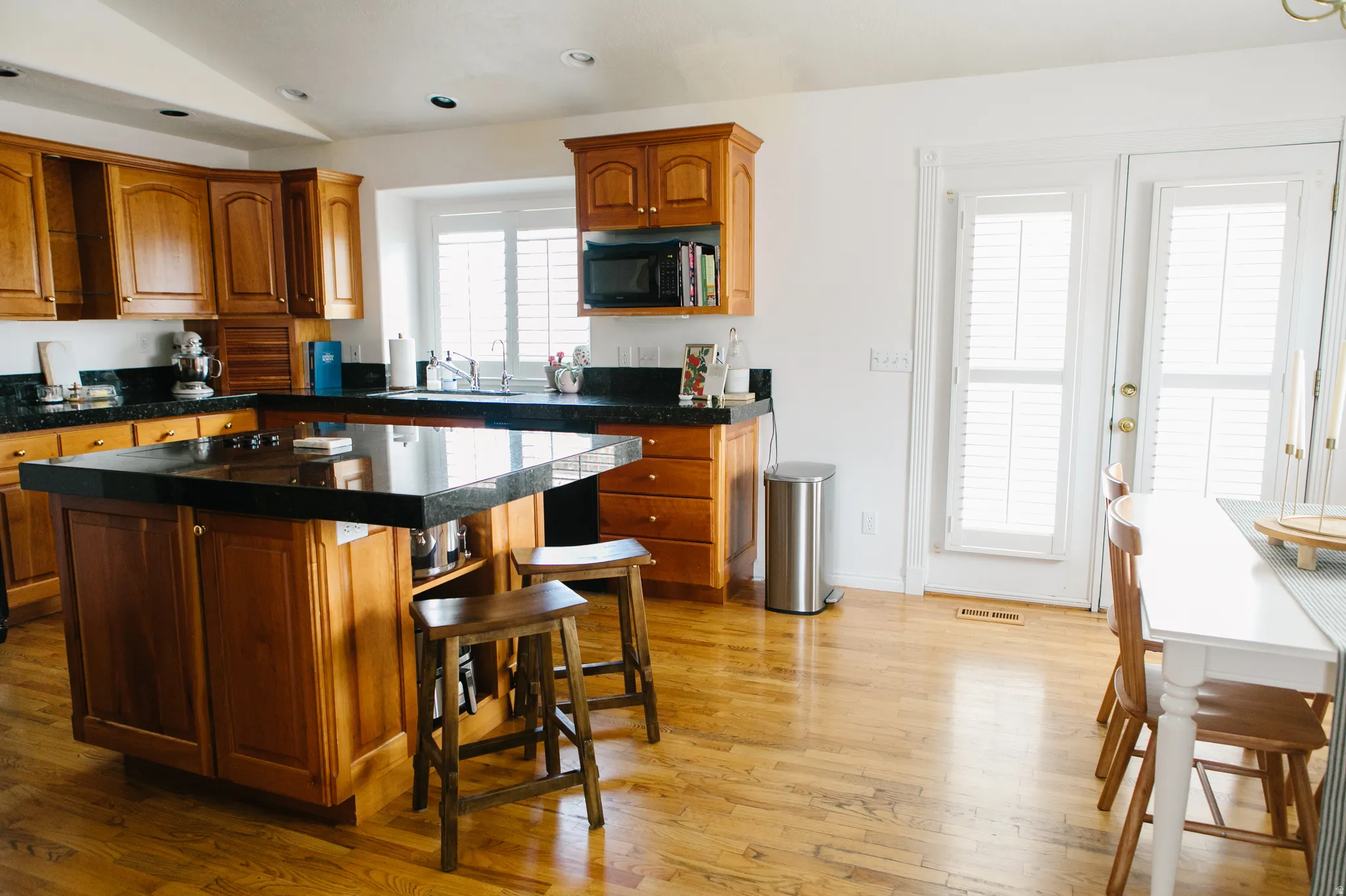 Kitchen featuring custom wood cabinetry, marble countertops, a central island with seating, a built-in microwave, and wood flooring