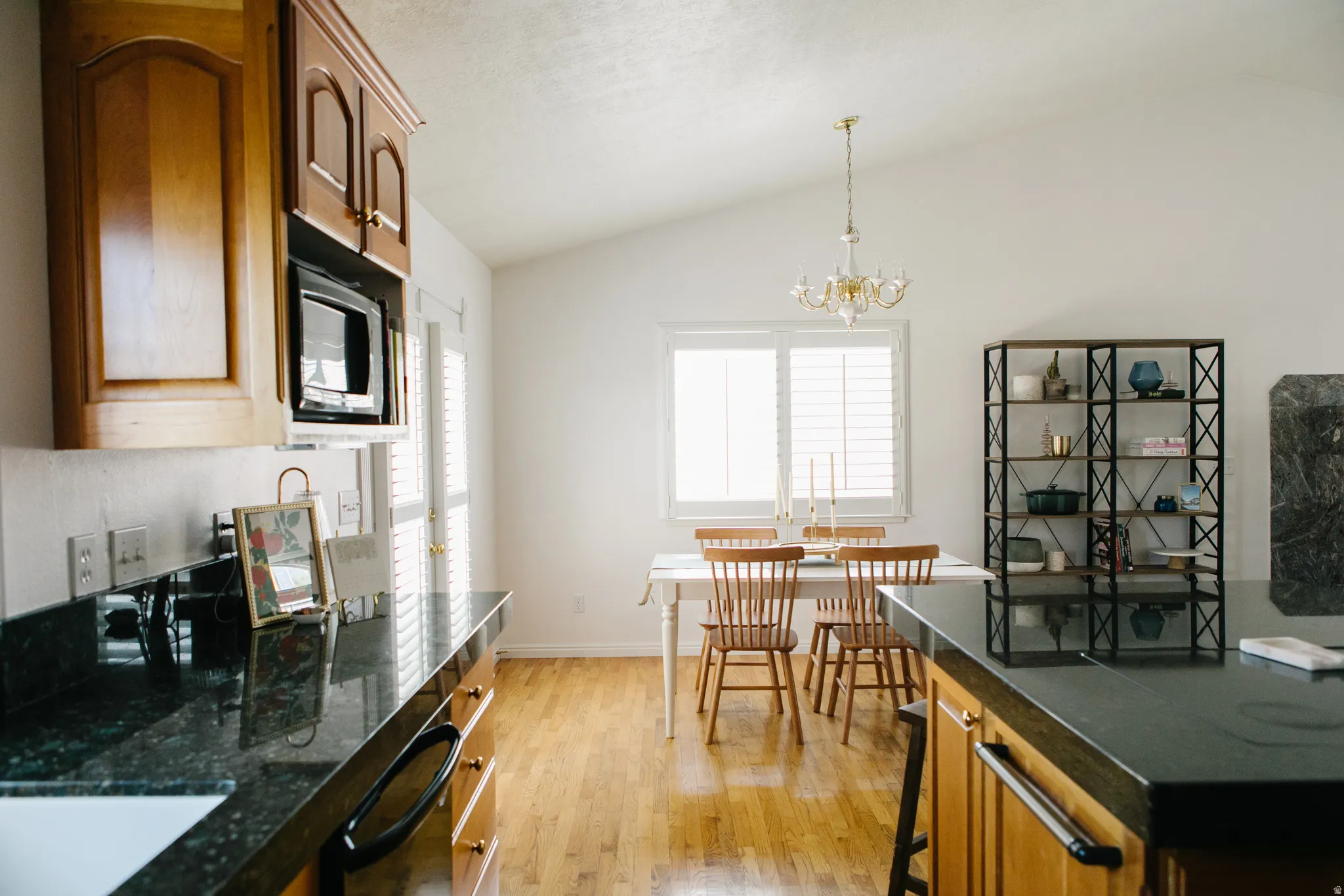 Kitchen and dining area featuring vaulted ceilings, wood-finish flooring, marble countertops, wood cabinetry, and a window with plantation shutters
