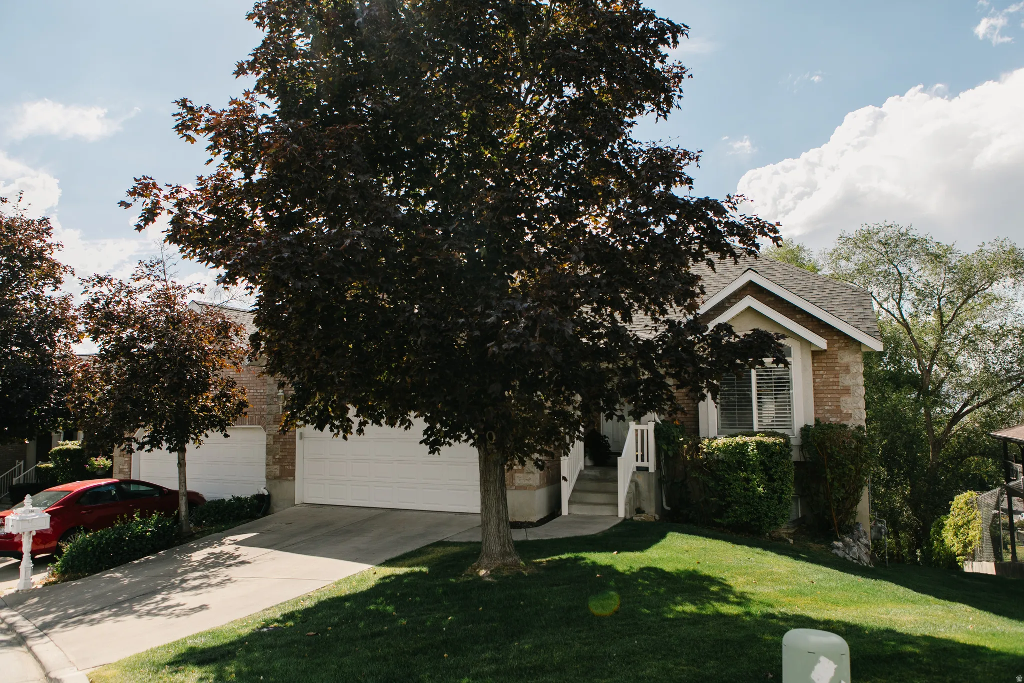 Two-car garage with white doors, sloped driveway, mature trees, and a manicured lawn