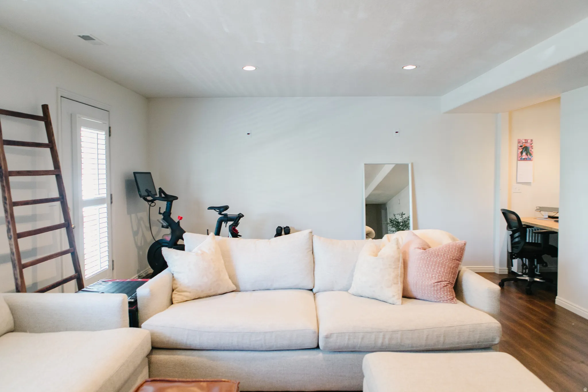 Recessed lighting illuminates this space featuring wood-finish flooring and a white paneled door with louvered blinds