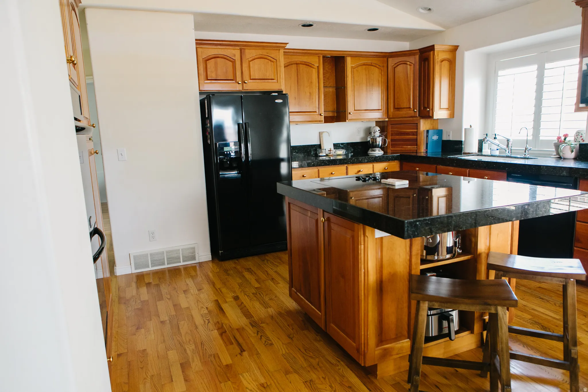 Kitchen featuring wood flooring, ample wood cabinetry, granite countertops, a large center island with seating, and a black side-by-side refrigerator